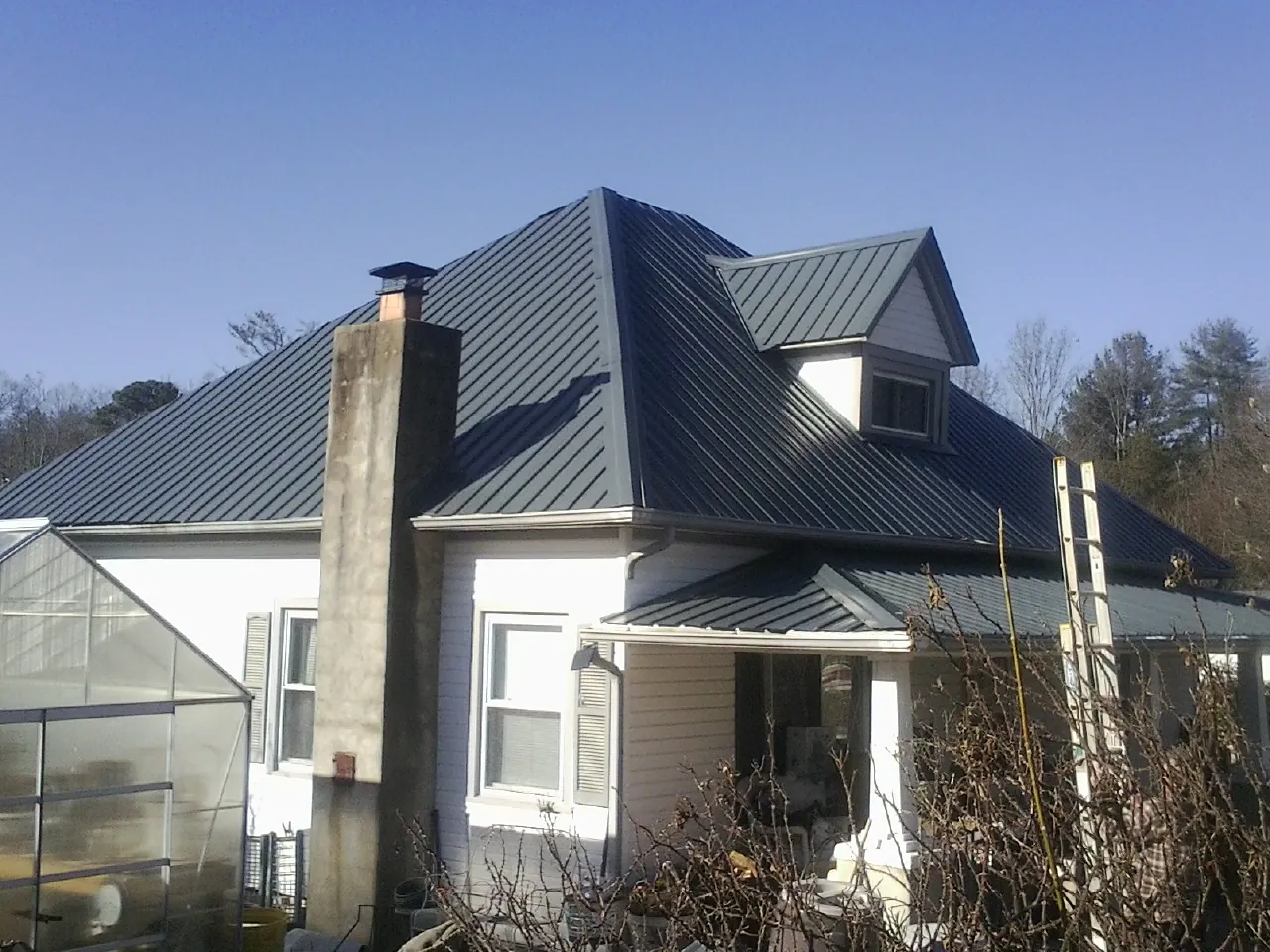 Dark blue standing seam metal roof on a white farmhouse with dormer — Slate & Tile Roof Repair by Roofing Brothers in Berry Creek