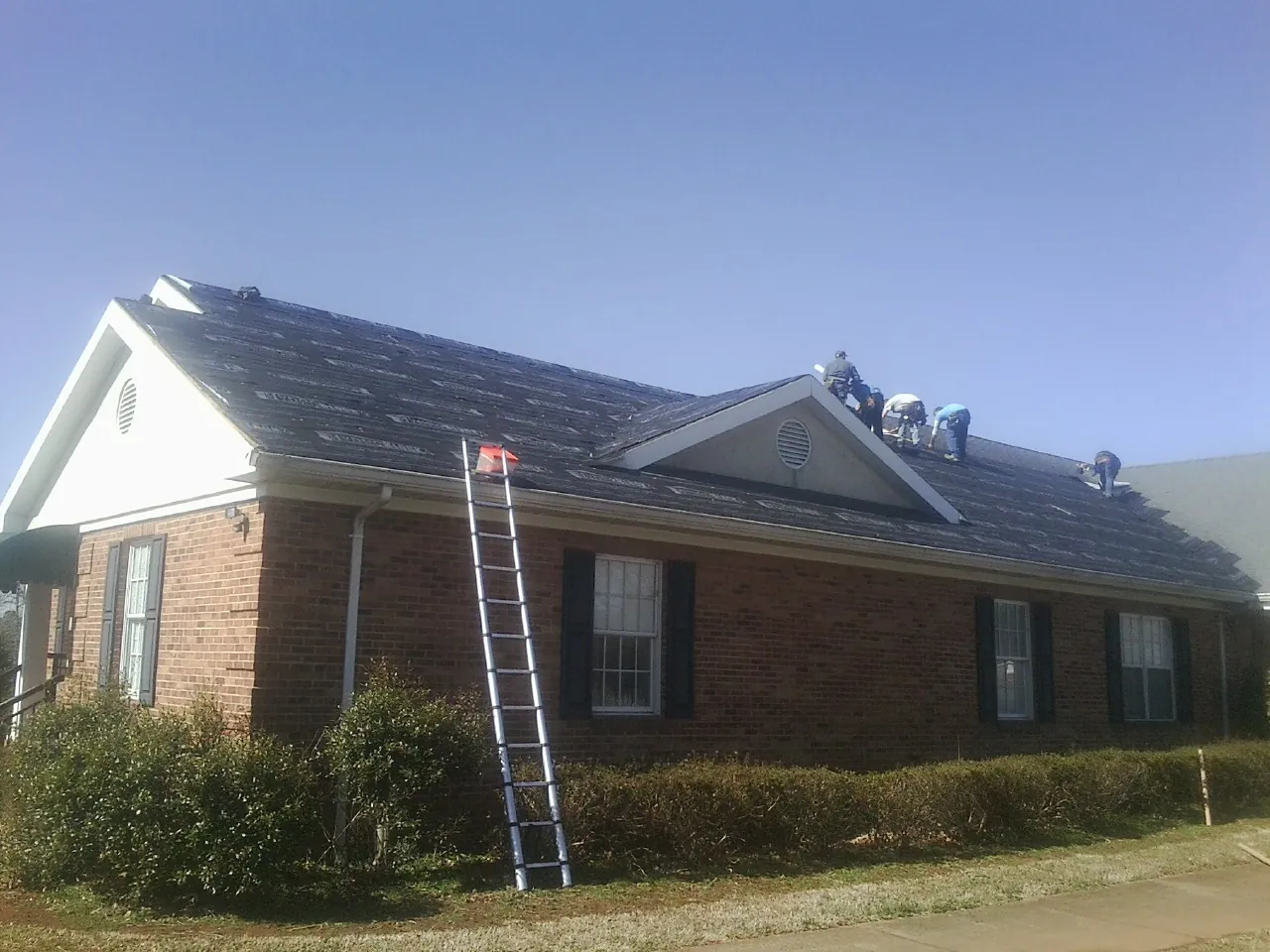 Crew tearing shingles off a brick ranch roof with a ladder set — Emergency Roof Repair work by our crew in Berry Creek