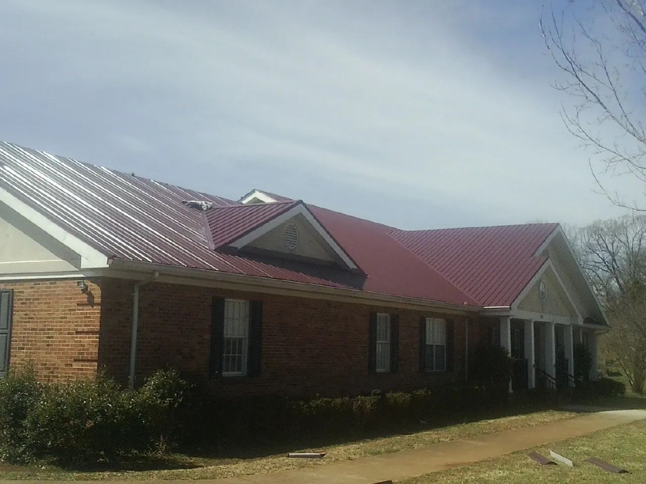 Red metal roof with gabled entries on a long brick building, from a Hail Damage Roof Repair job in Berry Creek