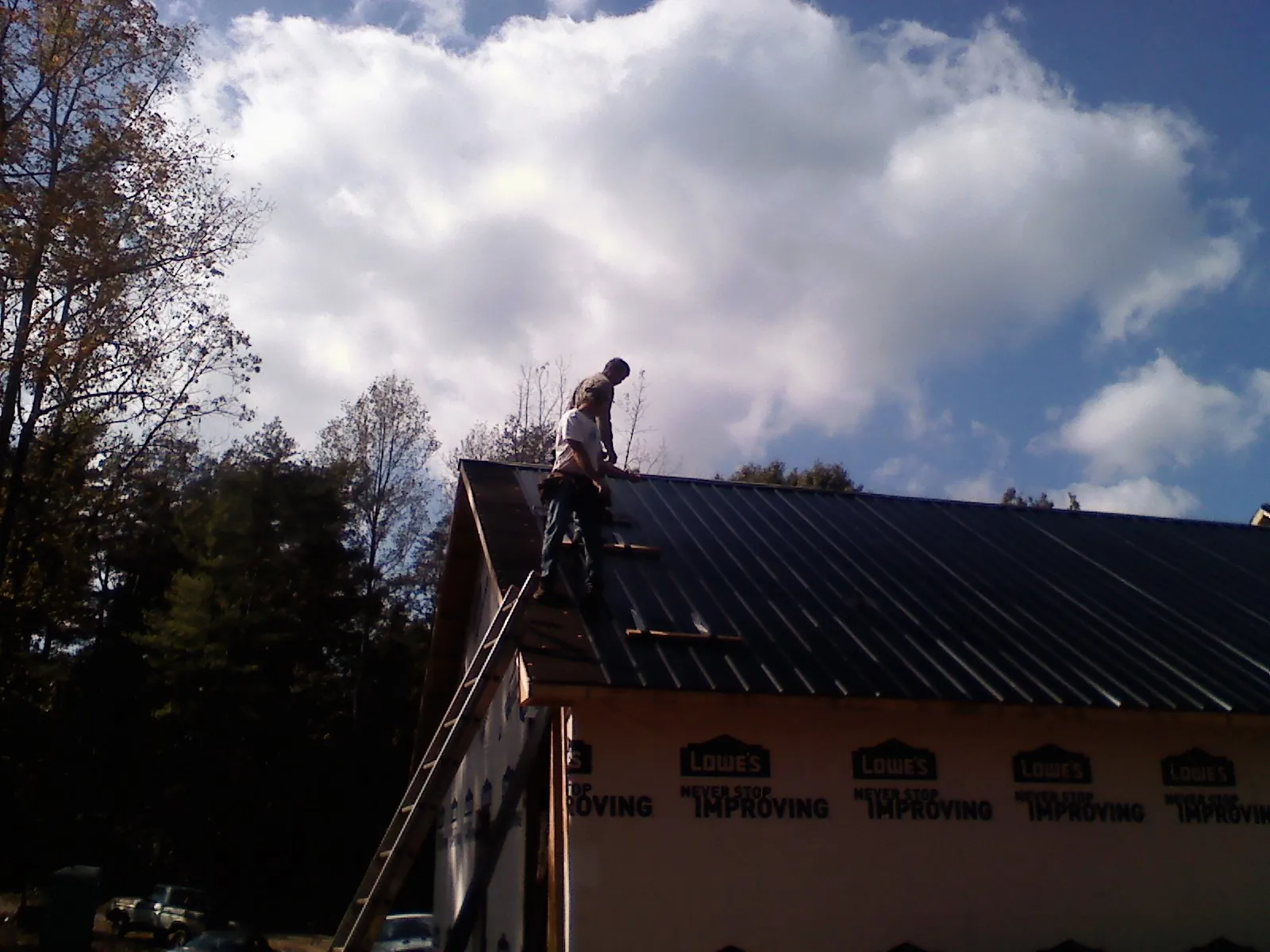 Roofer fastening dark metal panels high against a cloudy sky, from a Roof Inspection job in Berry Creek