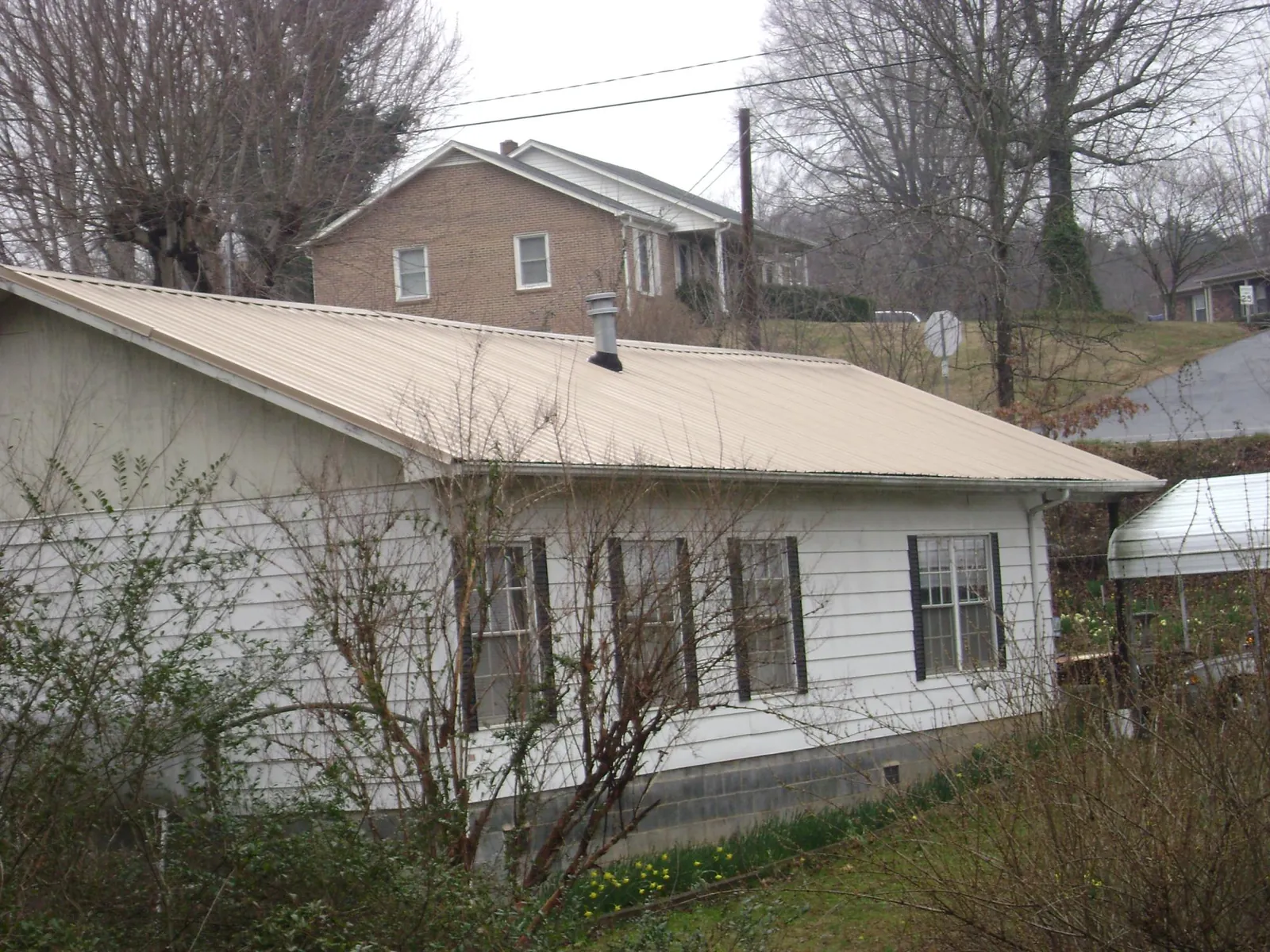 Tan metal roof on a white sided house set into a hillside — Commercial Roofing by Roofing Brothers in Berry Creek